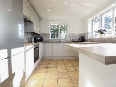 A kitchen with white cabinets a wooden countertop a toaster kettle microwave oven and flowers on the window sill at Surf Break in Polzeath