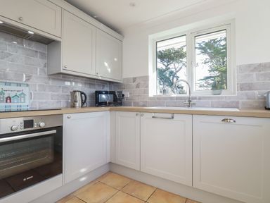 A kitchen with light gray cabinets a wooden countertop a oven microwave kettle and a window showing trees at Surf Break in Polzeath