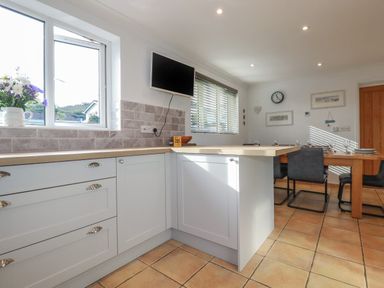 A kitchen with light blue cabinets a wooden countertop a wall-mounted television and a dining table with chairs at Surf Break in Polzeath