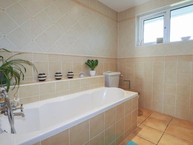 A bathroom with a bathtub a toilet and decorative candles on a tiled ledge at Surf Break Polzeath