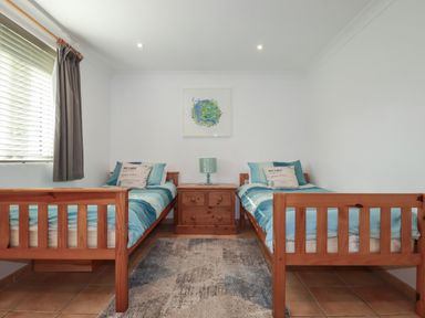 A bedroom with two single wooden beds blue bedding a bedside table and a lamp at Surf Break in Polzeath