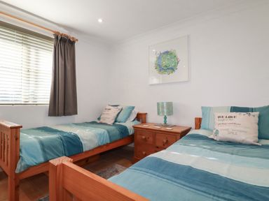 A bedroom with two single beds and a wooden nightstand with a lamp at Surf Break in Polzeath