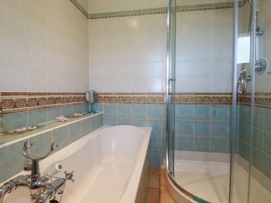 A bathroom with a bathtub and a glass shower enclosure with tiled walls at Surf Break in Polzeath