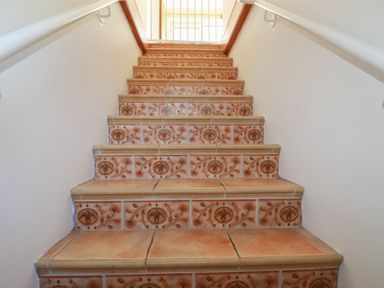A staircase with decorative floral tiles on the risers and beige tiles on the treads with white walls and handrails at Surf Break in Polzeath