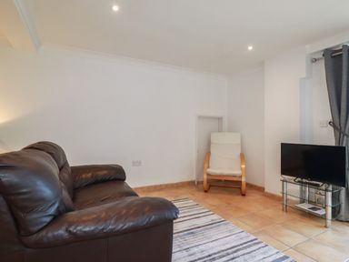 A living room with a brown leather sofa a cream armchair a striped rug and a TV on a glass stand at Surf Break in Polzeath