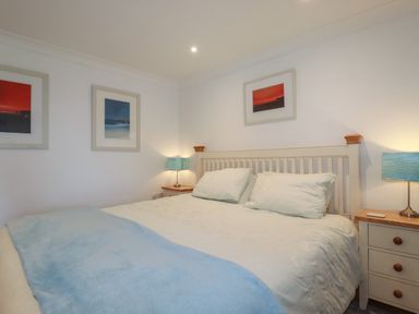 A bedroom with a double bed two bedside tables and three framed pictures on the walls at Surf Break in Polzeath