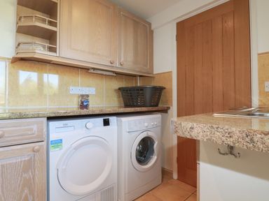 A laundry room with a washing machine dryer under a countertop wooden cabinets and a laundry basket on the counter at Surf Break in Polzeath