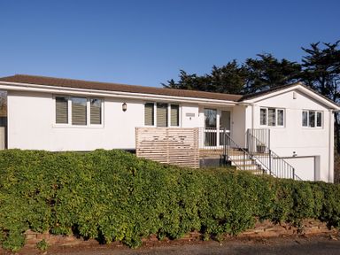 A white single-story house with multiple windows and a staircase leading to the front door at Surf Break in Polzeath