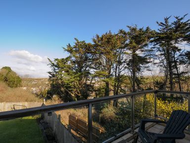 A balcony with a chair overlooking trees and a fenced yard at Surf Break in Polzeath