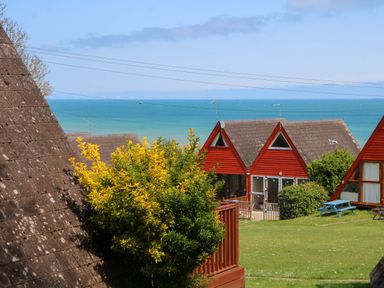 A seaside view with red A-frame houses green grass and bushes at Chalet 58 - The Beach House in Kingsdown