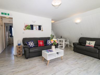 A living room with two black sofas, a white coffee table with flowers, and a small dining table at Chalet 58 - The Beach House in Kingsdown