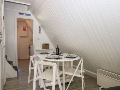 A dining area with a round table set for four with white chairs under a slanted ceiling at Chalet 58 - The Beach House Kingsdown