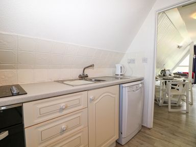 A kitchen with a sink kettle dishwasher and countertop looking into a dining area at Chalet 58 - The Beach House in Kingsdown