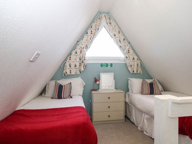 A bedroom with two single beds a small chest of drawers and a window with curtains at Chalet 58 - The Beach House in Kingsdown