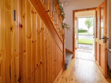 A hallway with wooden staircase and open door leading outside at 46 Dunalinn in Culdaff County Donegal