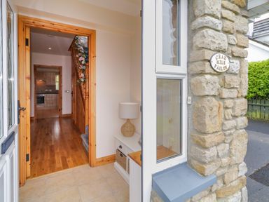 An entrance hallway with wooden floor and stairs decorated with flowers at 46 Dunalinn in Culdaff County Donegal
