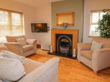 A living room with beige armchairs a fireplace and a wall-mounted television at 46 Dunalinn in Culdaff County Donegal