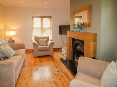 A living room with beige sofas a wooden floor a window with blinds and a fireplace at 46 Dunalinn in Culdaff County Donegal