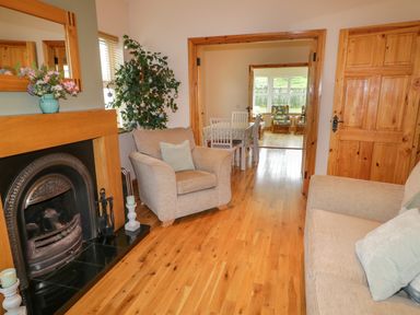 A living room with a fireplace armchairs and a view into a dining area at 46 Dunalinn in Culdaff County Donegal