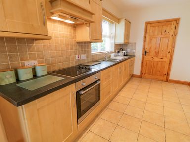 A kitchen with wooden cabinets black countertop stove oven sink and a wooden door at 46 Dunalinn in Culdaff County Donegal