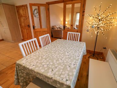 A dining area with a table covered with a floral tablecloth and white chairs next to a lighted decorative tree at 46 Dunalinn in Culdaff County Donegal