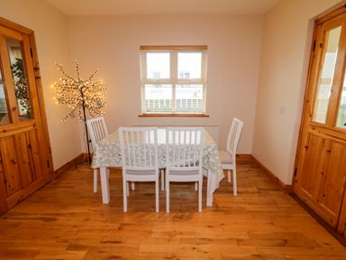 A dining room with a table and four chairs next to a window and a lighted decorative tree at 46 Dunalinn in Culdaff County Donegal