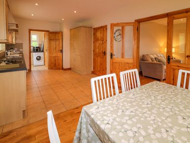 A kitchen with dining table and chairs washing machine in a utility area and a living room with sofa at 46 Dunalinn in Culdaff County Donegal