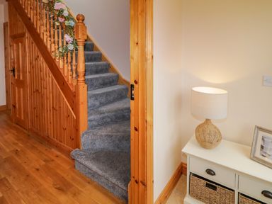 A hallway with wooden staircase with grey carpet and a white table with a lamp at 46 Dunalinn in Culdaff County Donegal