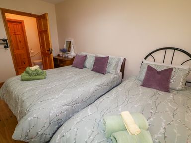 A bedroom with two beds green floral bedding purple pillows wooden dresser and an open door showing a bathroom at 46 Dunalinn in Culdaff County Donegal