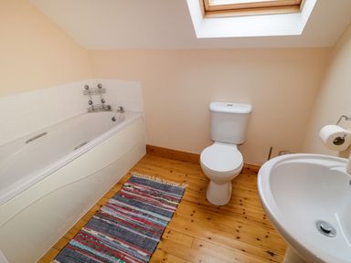 A bathroom with a bathtub toilet sink a skylight and a striped rug on a wooden floor at 46 Dunalinn in Culdaff County Donegal
