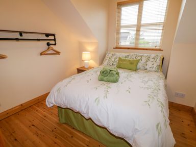 A bedroom with a double bed with green and white bed linens two rolled towels on the bed a wooden floor a window with blinds and a bedside table with a lamp at 46 Dunalinn in Culdaff County Donegal