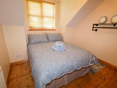 A bedroom with a double bed covered with light blue bedding and towels stacked on top at 46 Dunalinn in Culdaff County Donegal