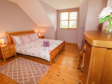 A bedroom with a wooden bed and floral bedding two bedside tables with lamps a window wooden floor and a wooden chest of drawers with a flower vase at 46 Dunalinn in Culdaff County Donegal