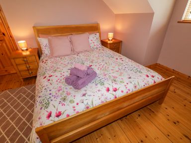 A bedroom with a wooden bed with floral bedding two bedside tables with lamps and folded towels on the bed at 46 Dunalinn in Culdaff County Donegal