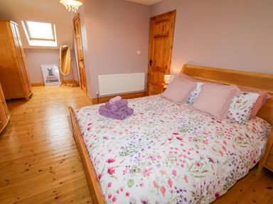 A bedroom with a wooden bed with floral bedding folded towels on the bed wooden furniture a standing mirror and a skylight window at 46 Dunalinn in Culdaff County Donegal