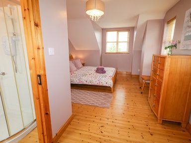 A bedroom with a bed and dresser with wooden floors and a bathroom shower at 46 Dunalinn in Culdaff County Donegal