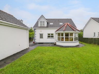 A backyard with green grass and a white house with a glass enclosed patio at 46 Dunalinn in Culdaff County Donegal