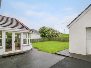 A backyard with a lawn, paved areas, a white building with glass doors, and a garage at 46 Dunalinn in Culdaff County Donegal