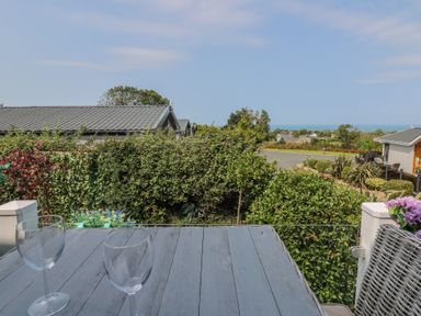 An outdoor area with glasses on a table and a view of houses and ocean at Coogee View Maenygroes near New Quay
