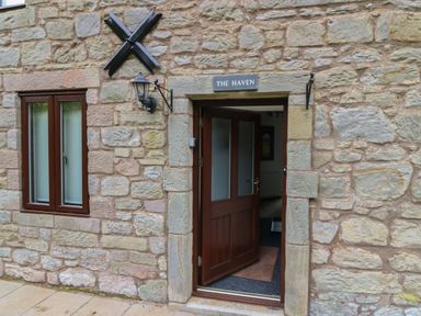An open wooden door and window on a stone wall with a sign above the door saying The Haven in Norham