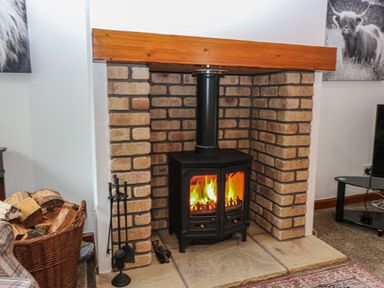 A burning wood stove with a brick surround and wooden beam mantel at The Haven in Norham