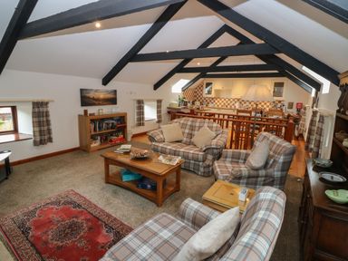 A living room with plaid sofas a wooden coffee table and bookshelves under exposed ceiling beams at The Haven in Norham
