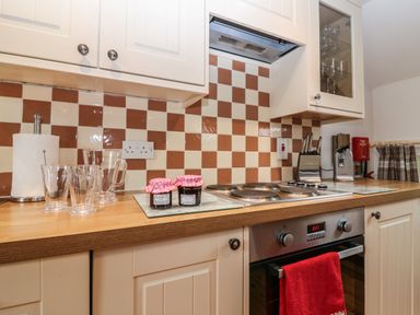 A kitchen countertop with glasses paper towel electric stove and oven jars of jam and knife block at The Haven in Norham