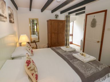 A bedroom with a bed with floral pillows a wooden wardrobe a lamp and a mirror at The Haven in Norham