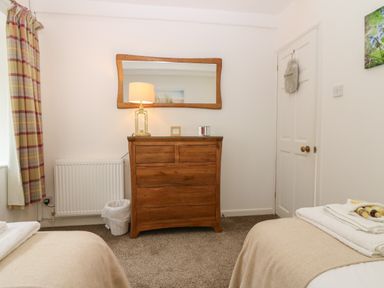 A bedroom with two single beds a wooden dresser with a lamp and mirror at The Haven in Norham