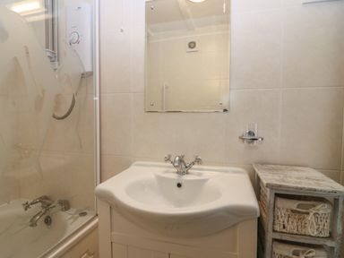 A bathroom with a sink mirror shower and a wooden storage unit with baskets at The Haven in Norham