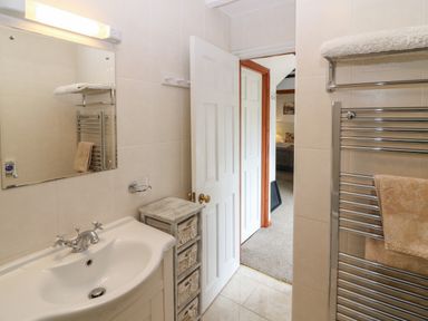 A bathroom with a sink mirror towel rack and open door leading to a carpeted room at The Haven in Norham