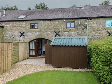 A stone house with a brown shed and green lawn with a gravel path at The Haven in Norham
