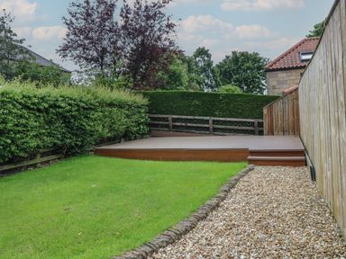 A backyard with a wooden deck a gravel path a green lawn and fences at The Haven in Norham