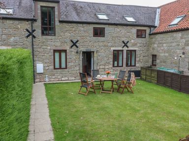 A stone house with multiple windows and a lawn with a table and chairs at The Haven in Norham